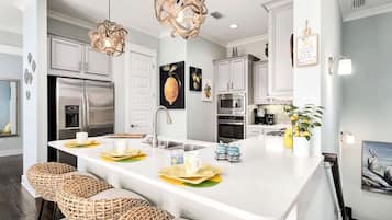 Una cocina moderna con armarios blancos, electrodomésticos de acero inoxidable y una isla central con taburetes de bar.
