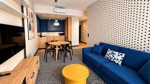 A modern living room with a blue sofa, a wooden dining table, and a kitchen in the background. - Cobalt36 (Bolesławiec)