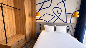 Une chambre d’hôtel avec un lit, une armoire en bois et un mur orné de lignes bleues abstraites.