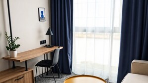 A modern hotel room with a desk, chair, sofa, and a round coffee table. - Cobalt36 (Bolesławiec)
