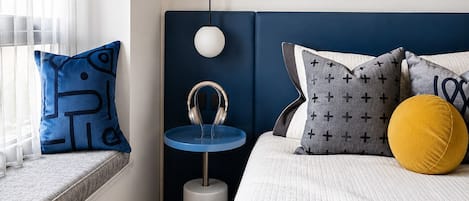 Un dormitorio con cama, almohadas, una mesita de noche y una ventana.