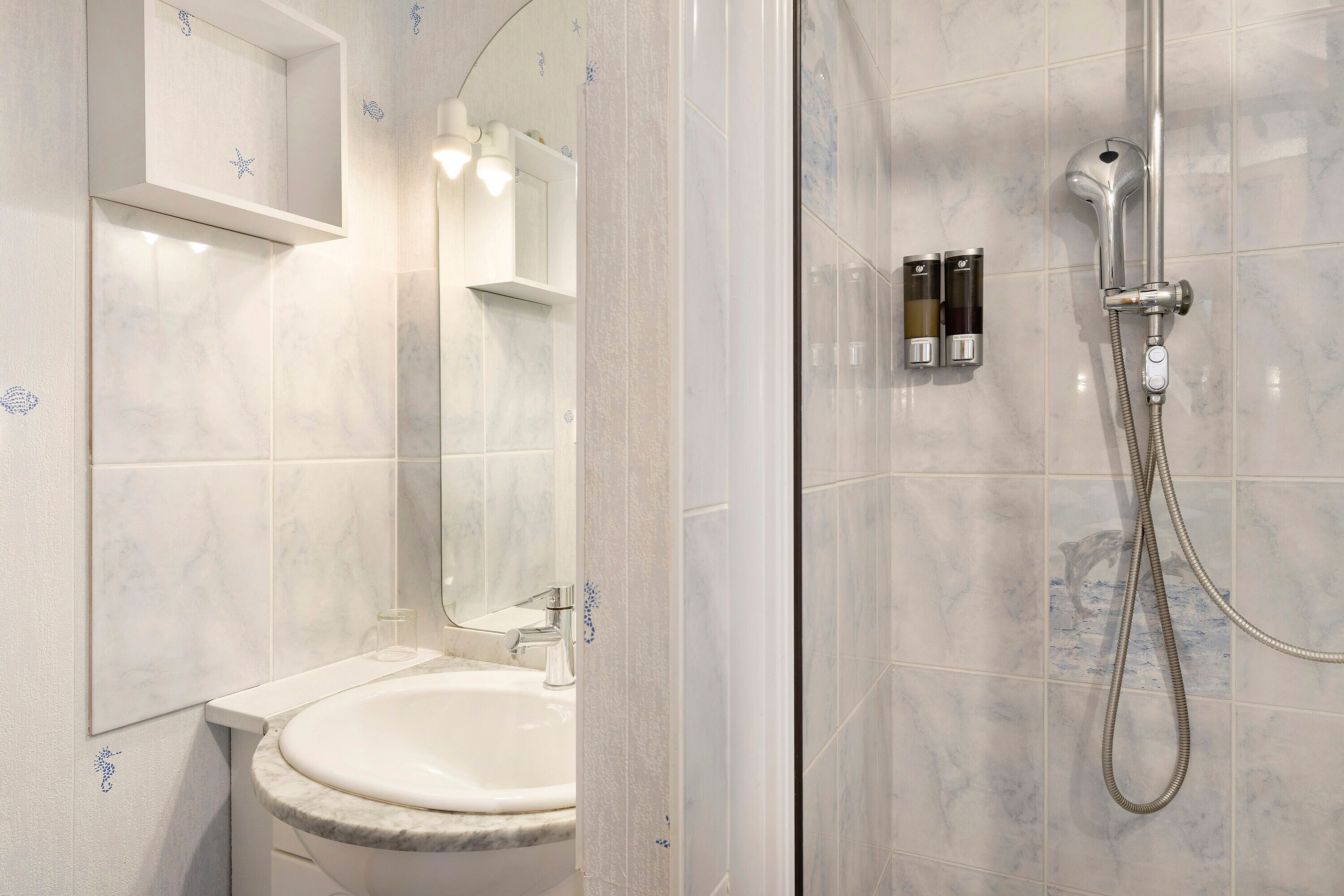 A bathroom with a sink, mirror, shower, and tiled walls.