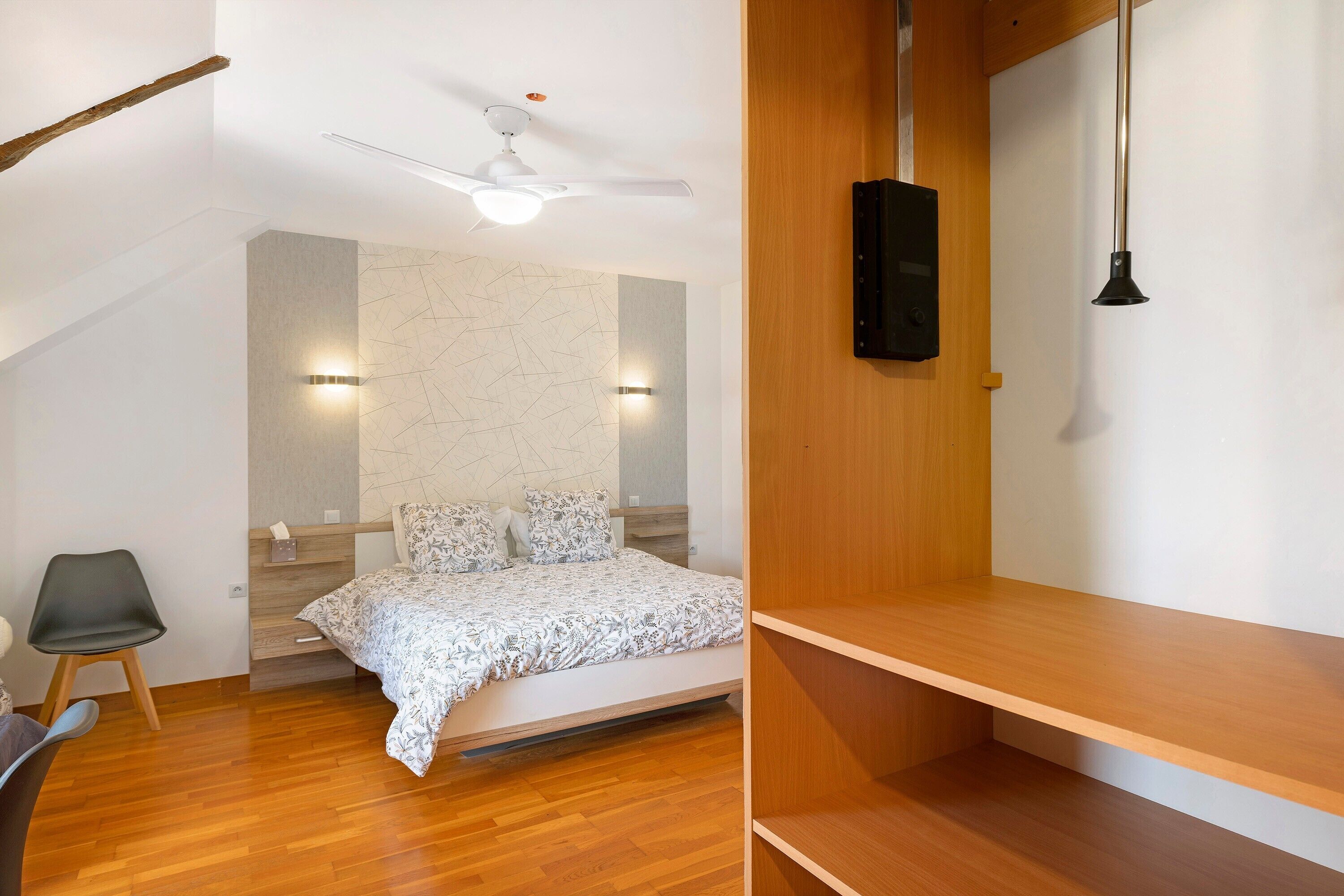 Een moderne slaapkamer met een bed, een plafondventilator en een houten plank.