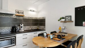 A modern kitchen with a built-in oven, a coffee maker, and a dining table with chairs. - Guest Room “Le clair de Lune” with Shared Terrace & Garden, Wi-Fi (Romillé)