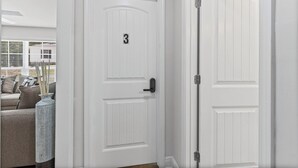 A white door with a number '3' and a keypad lock, a white door with a latch, and a beige sofa with cushions. - The Compound (Mobile)