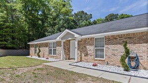 A two-story brick house with a covered porch, a front door, and a visible garage door. - The Compound (Mobile)