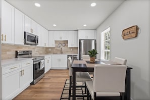 Una cocina moderna con armarios blancos, electrodomésticos de acero inoxidable y una zona de comedor con mesa y sillas.