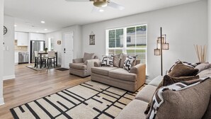 A living room with a sofa, a dining area with chairs, a kitchen with appliances, and a ceiling fan. - The Compound (Mobile)