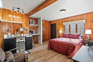 Ein gemütliches Blockhauszimmer mit Bett, Schreibtisch, Küchenzeile und Fenster.
