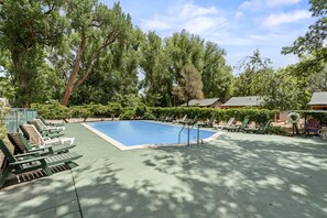 Ein rechteckiger Pool, umgeben von grünen Liegestühlen und einer gepflasterten Liegefläche.