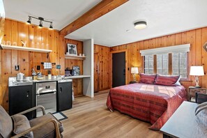 Ein gemütliches Blockhauszimmer mit Bett, Schreibtisch, Küchenzeile und Fenster.