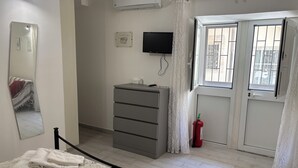 A bedroom with a bed, a dresser, a television, and a fire extinguisher. - DIONE: A cozy, fully equipped apartment in the heart of Ortigia, Syracuse (Siracusa)