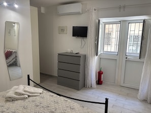 A bedroom with a bed, a dresser, a television, and a fire extinguisher. - DIONE: A cozy, fully equipped apartment in the heart of Ortigia, Syracuse (Siracusa)