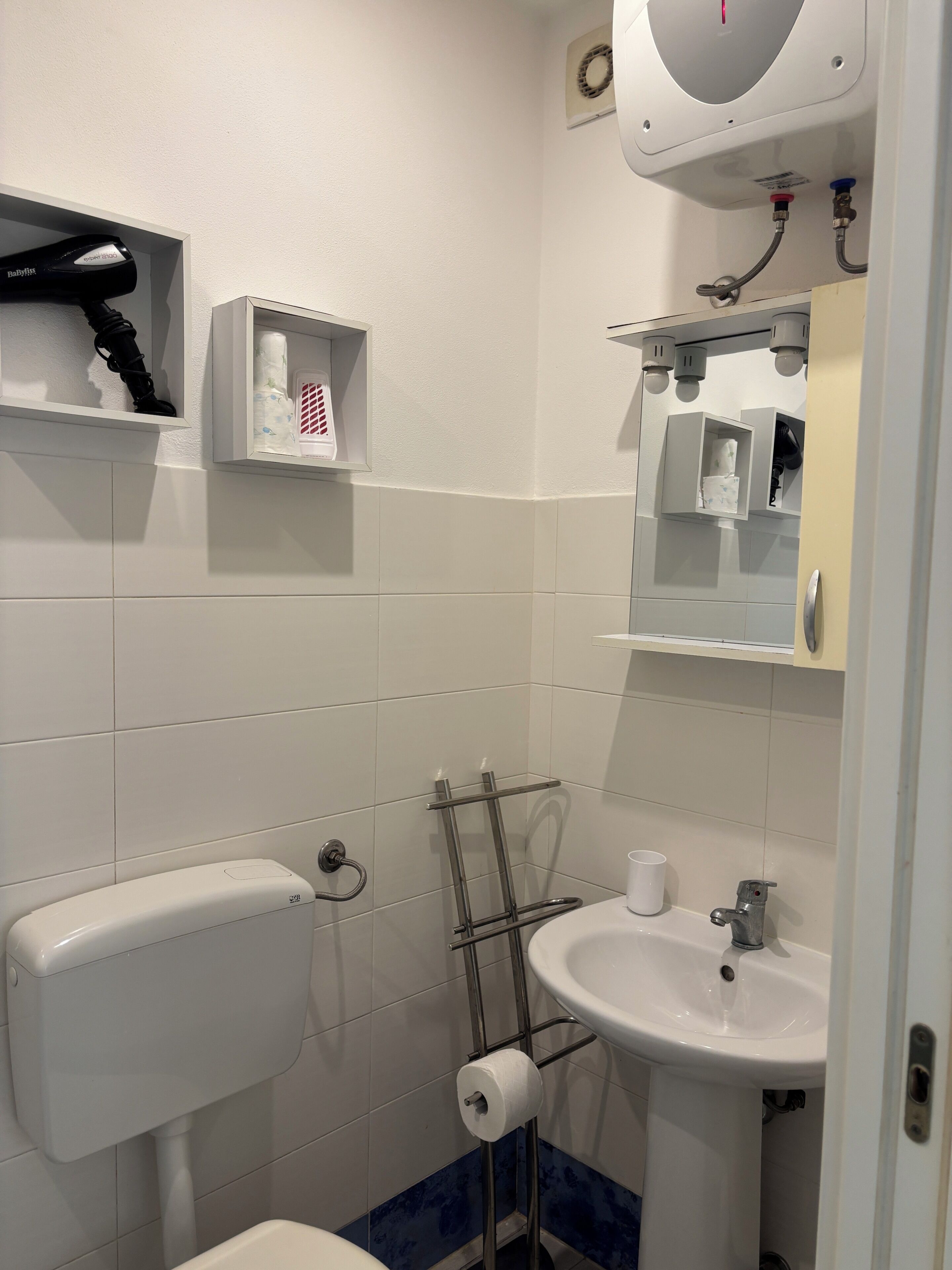 Un baño con inodoro, lavamanos, perchero para toallas y espejo.