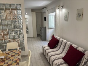 A room with a striped sofa, a dining table with a floral tablecloth, and a wall with patterned glass panels. - DIONE: A cozy, fully equipped apartment in the heart of Ortigia, Syracuse (Siracusa)