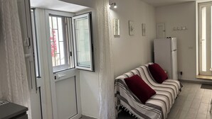 A room with a sofa, a refrigerator, a door with a window, and a wall with framed pictures. - DIONE: A cozy, fully equipped apartment in the heart of Ortigia, Syracuse (Siracusa)