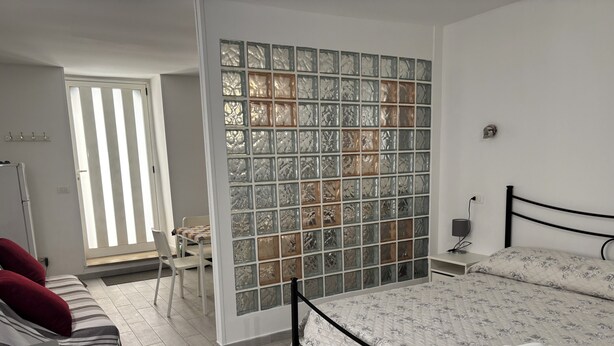 A bedroom with a bed, a chair, a desk, and a glass partition wall. - DIONE: A cozy, fully equipped apartment in the heart of Ortigia, Syracuse (Siracusa)