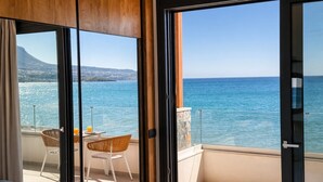 Een balkon met een tafel, stoelen, een glazen deur en uitzicht op zee en een berg.