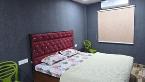 Un dormitorio con una cama, un sillón verde, aire acondicionado de pared y suelo estampado.