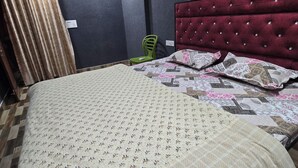 Un dormitorio con cama, cabecera roja, silla verde y cortina.