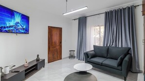 Ein modernes Wohnzimmer mit Flachbildfernseher, einem dunkelgrauen Sofa, einem runden Couchtisch und einer Holztür.