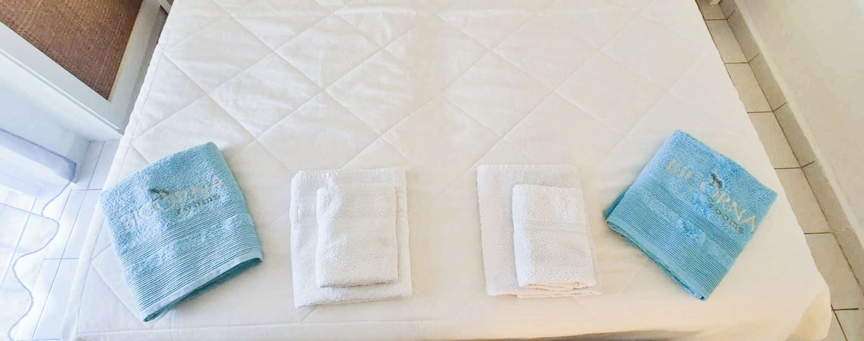 Una cama con un colchón blanco acolchado, dos toallas dobladas y una toalla azul al lado.