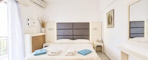 Ein Hotelzimmer mit Bett, Nachttischen, einem Spiegel, einem Fenster mit Vorhängen und einer Klimaanlage.