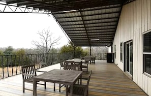Eine überdachte Terrasse im Freien mit Tisch und Stühlen, einem Geländer und Blick auf die umliegende Landschaft.