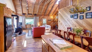 Un'ampia zona giorno con soffitto alto, travi in legno, un tavolo da pranzo con sedie, un divano rosso e un camino.