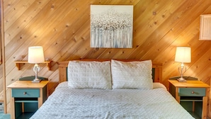Una camera da letto con soffitto in legno, un letto con biancheria bianca, due comodini con lampade e un quadro sopra il letto.