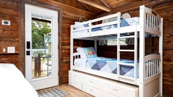 A cabin with a bunk bed, a door leading outside, and a small white dresser.