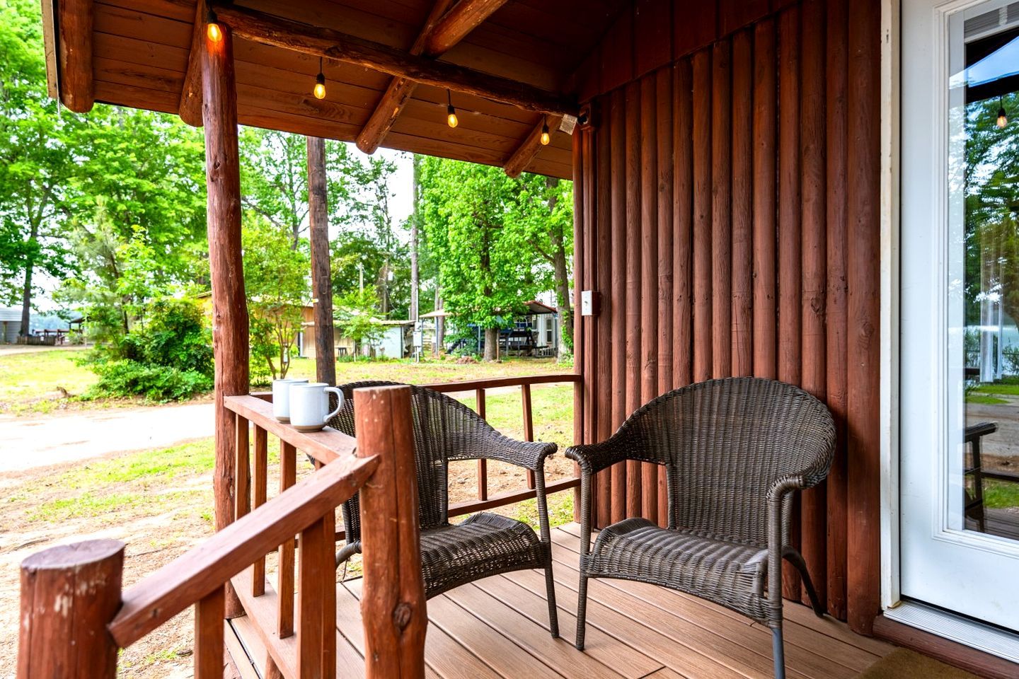 Une terrasse en bois, avec des chaises et une table en osier, donnant sur un espace verdoyant planté d’arbres.