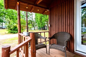 Una terraza de madera con sillas de mimbre y una mesa, con vistas a una zona verde con árboles.