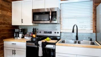 A compact kitchen with white cabinets, a stainless steel microwave, a stove, and a sink.