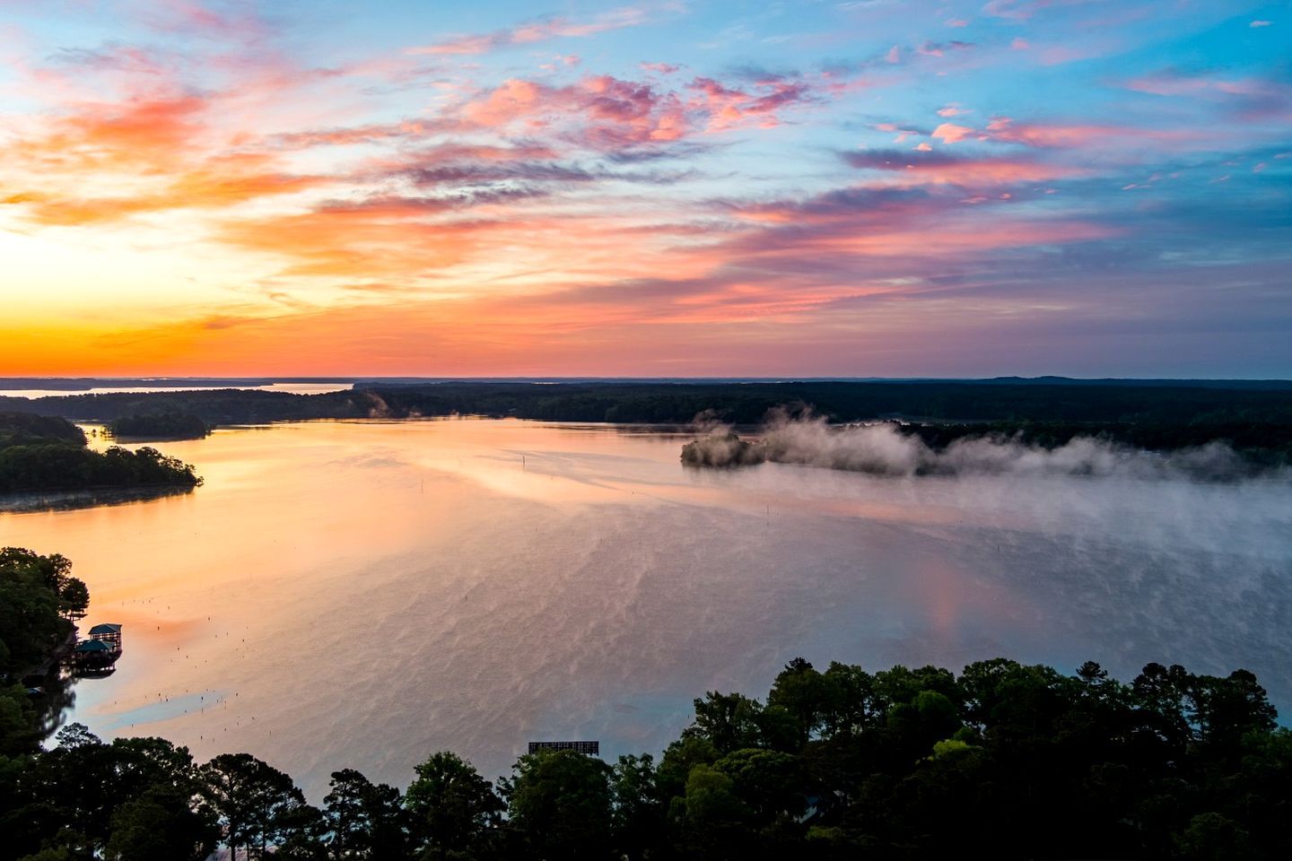 A wide river with a misty area, surrounded by dense forest and a clear sky.