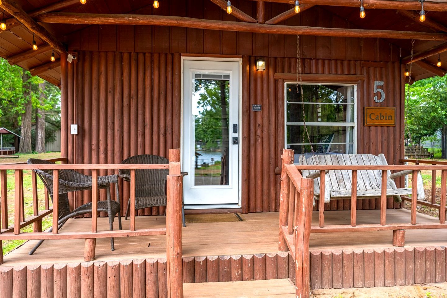 A cabin with a wooden exterior, a porch with wicker chairs, a swing, and a sign indicating it's cabin number 5.