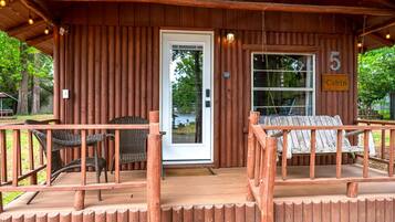 A cabin with a wooden exterior, a porch with wicker chairs, a swing, and a sign indicating it's cabin number 5.