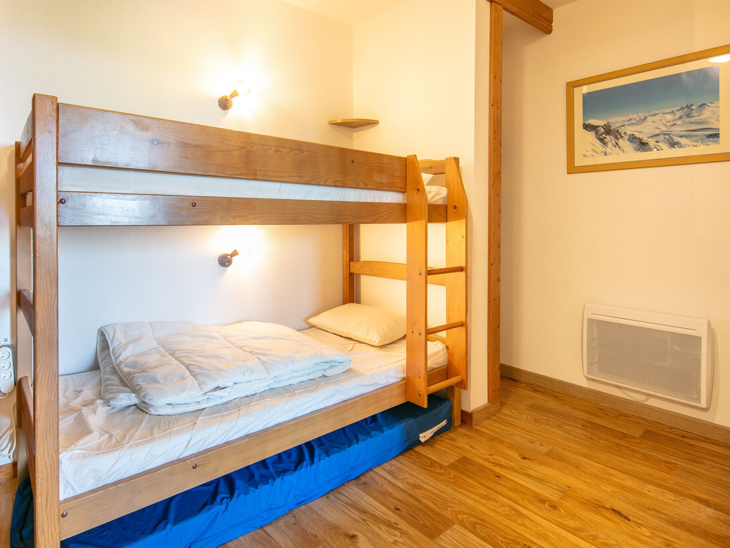 A bunk bed with a ladder, a wall-mounted light, and a framed picture on the wall.