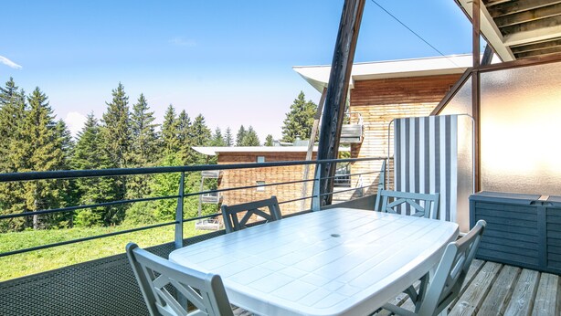 Un balcon avec une table et des chaises, donnant sur une zone boisée.