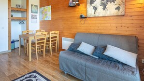 Un salon chaleureux avec un canapé gris, une table à manger en bois, des chaises et une œuvre d’art représentant une carte du monde accrochée au mur.
