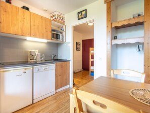 A compact kitchen with a dishwasher, coffee maker, and wooden cabinets. - Family apartment with a balcony and a view of the mountains (Chamrousse)