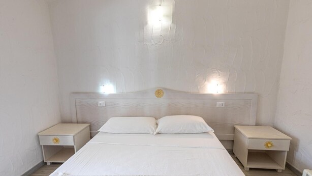 Une chambre à coucher avec un lit simple, deux tables de chevet et une tête de lit dotée d’un luminaire.