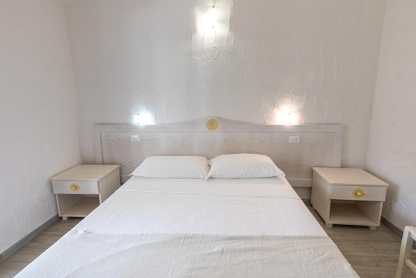 A bedroom with a single bed, two bedside tables, and a headboard with a light fixture.