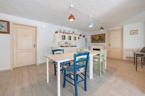 Zona de menjador amb taula i cadires de fusta, un armari blanc amb portes de vidre i un quadre a la paret.