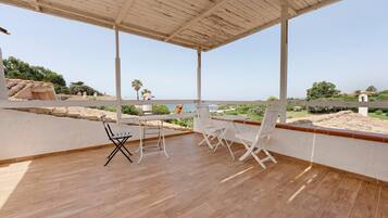 Un espacio al aire libre techado con suelo de madera, sillas de metal blanco y una mesa.