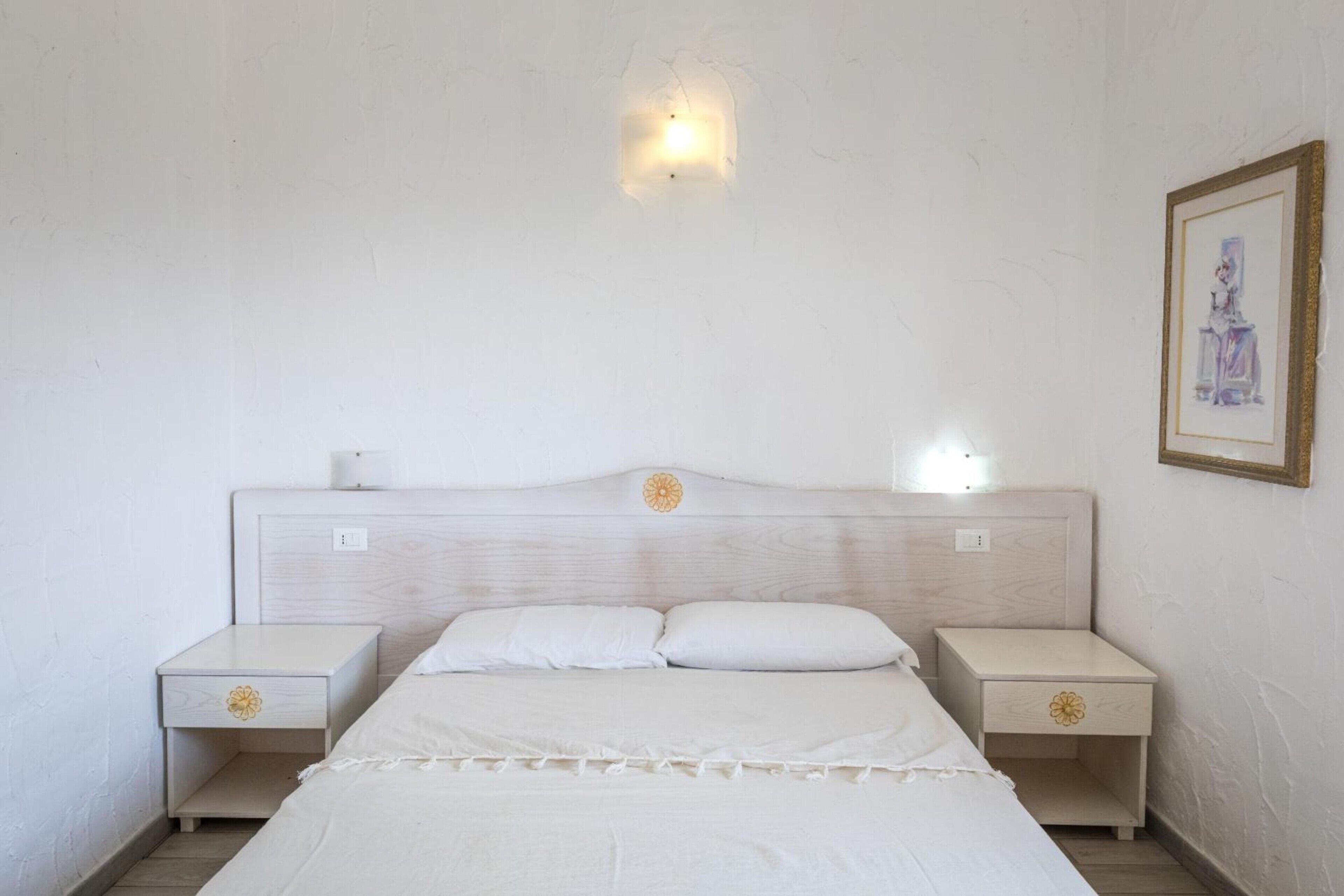 Una camera da letto con un letto, due comodini, una lampada a parete e un quadro incorniciato.