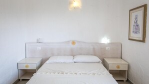 Une chambre à coucher avec un lit, deux tables de chevet, une lampe fixée au mur et un tableau encadré.
