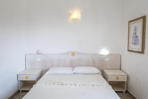 A bedroom with a bed, two nightstands, a wall-mounted light, and a framed picture.