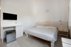 A bedroom with a bed, a TV mounted on the wall, a desk, and a nightstand.