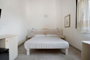 A bedroom with a bed, bedside tables, a desk, and a framed picture on the wall.
